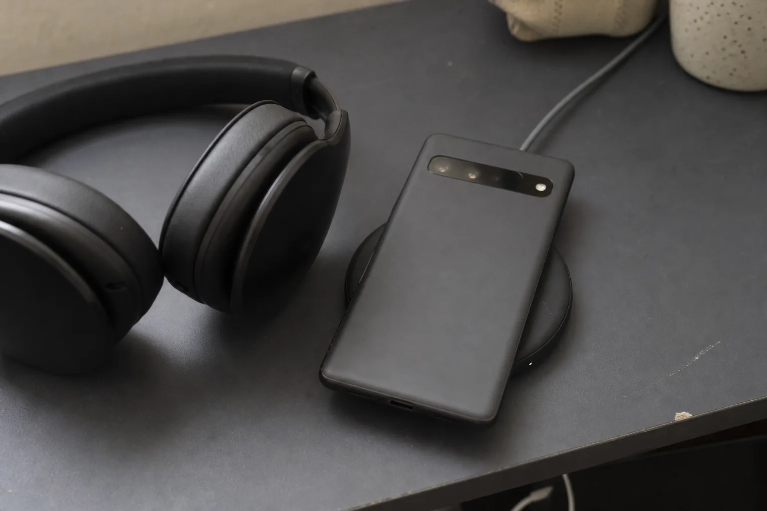 Android phone face‑down on a wireless charger next to over‑ear headphones on a desk.