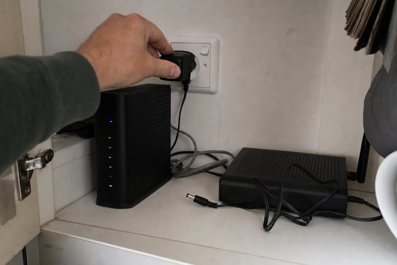 Hand plugging in a modem while the router plug remains unplugged nearby.